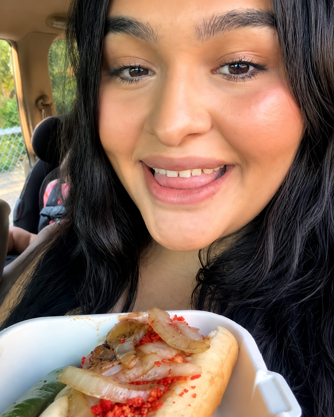 Customer showing off a grilled hot dog with onions and toppings